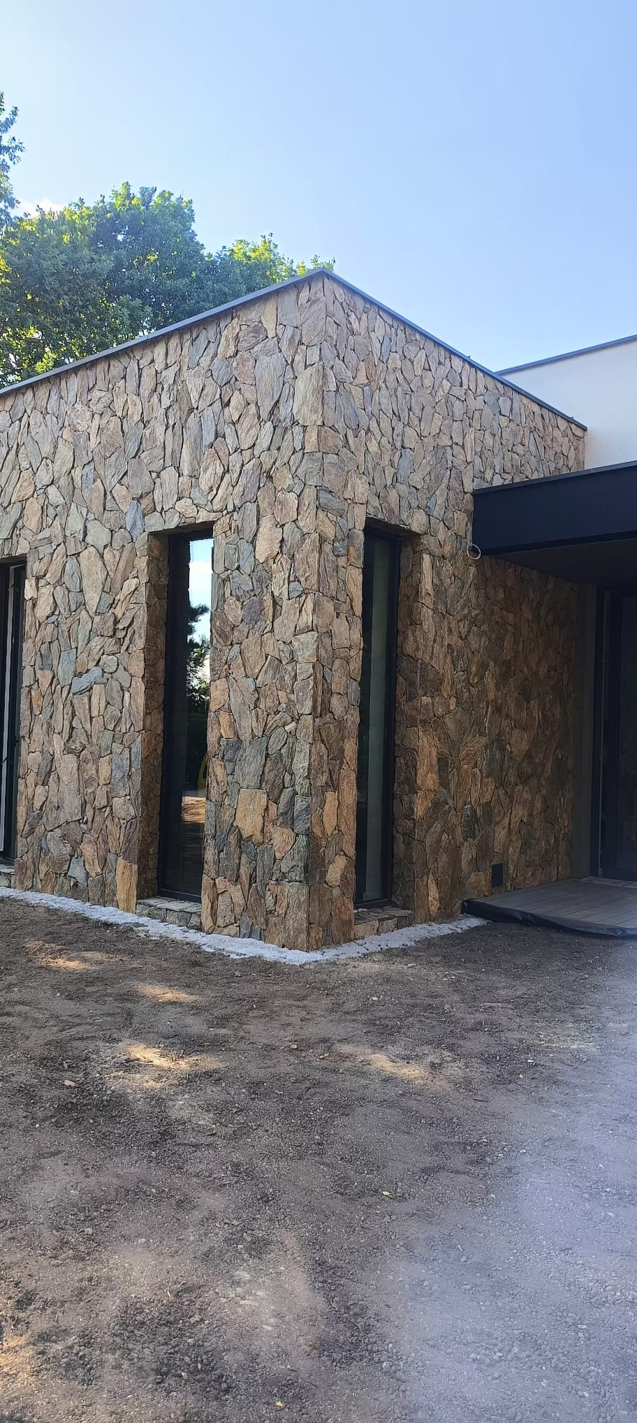 Elewacja budynku wykończona nieregularnym kamieniem naturalnym w odcieniach brązu i szarości, z widocznymi oknami i fragmentem tarasu.