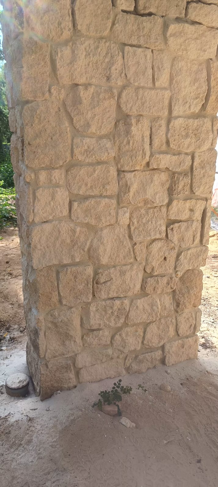 Fragment kolumny z piaskowca, zbudowanej z nieregularnych, ciosanych kamieni, widoczny na tle ziemi i zieleni.