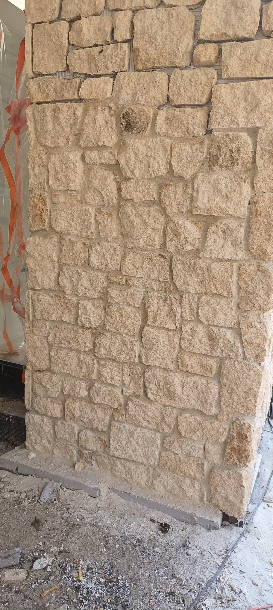 Ściana wykończona piaskowcem w trakcie montażu, widoczne pozostałości zaprawy i folia ochronna w tle.