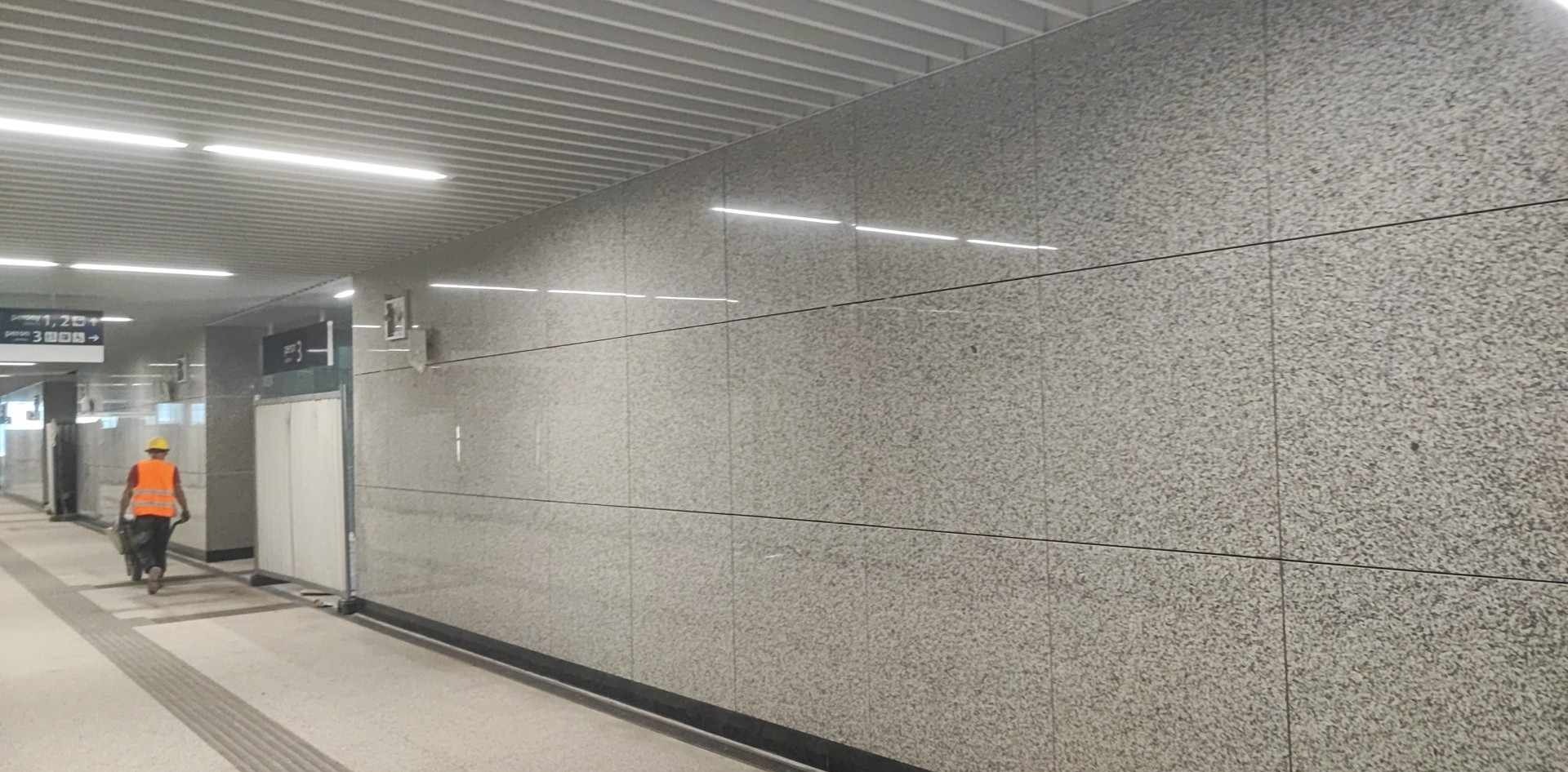 Korytarz w trakcie wykańczania z wyłożonymi płytami z szarego kamienia i pracownikiem budowlanym w oddali