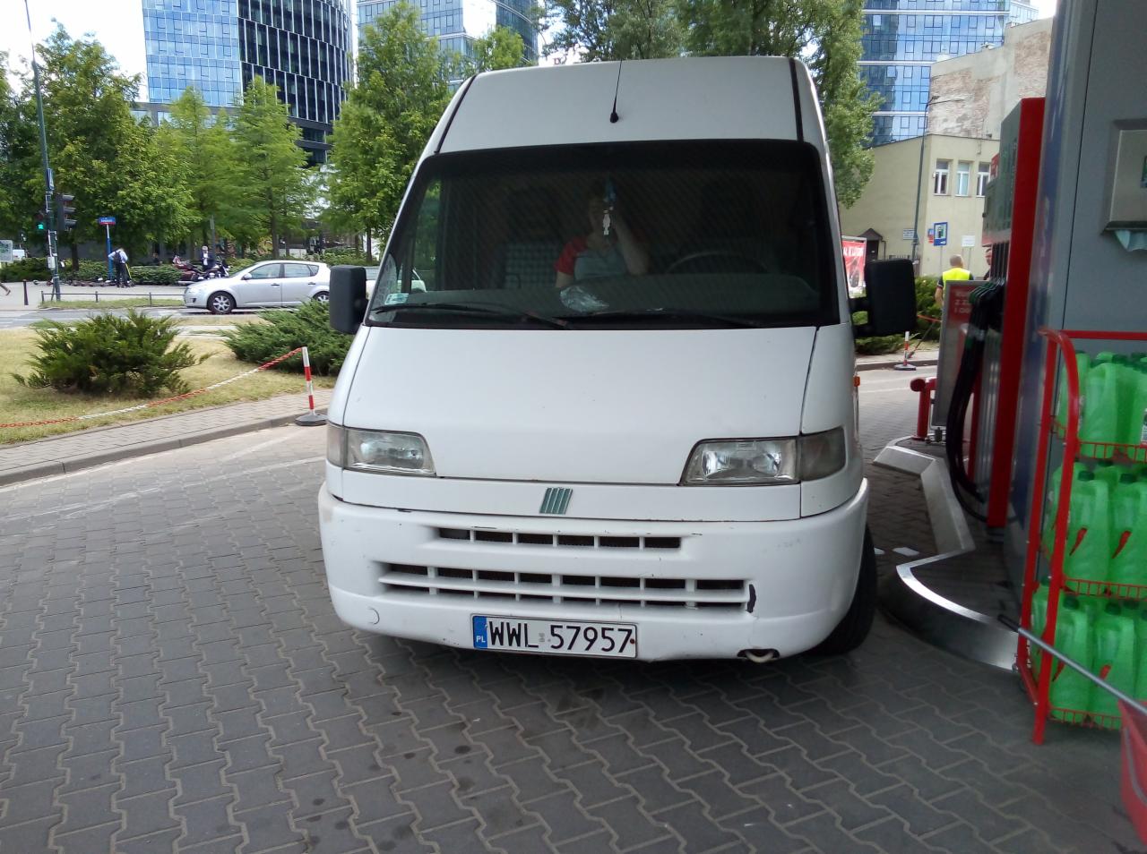 Biały bus Fiat Ducato z widoczną tablicą rejestracyjną WWL 57957, zatankowany na stacji benzynowej w miejskim otoczeniu.