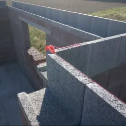 Wznoszenie ścian domu z bloczków betonowych i cegły ceramicznej, widoczne narzędzie murarskie - sznurek traserski z poziomnicą.