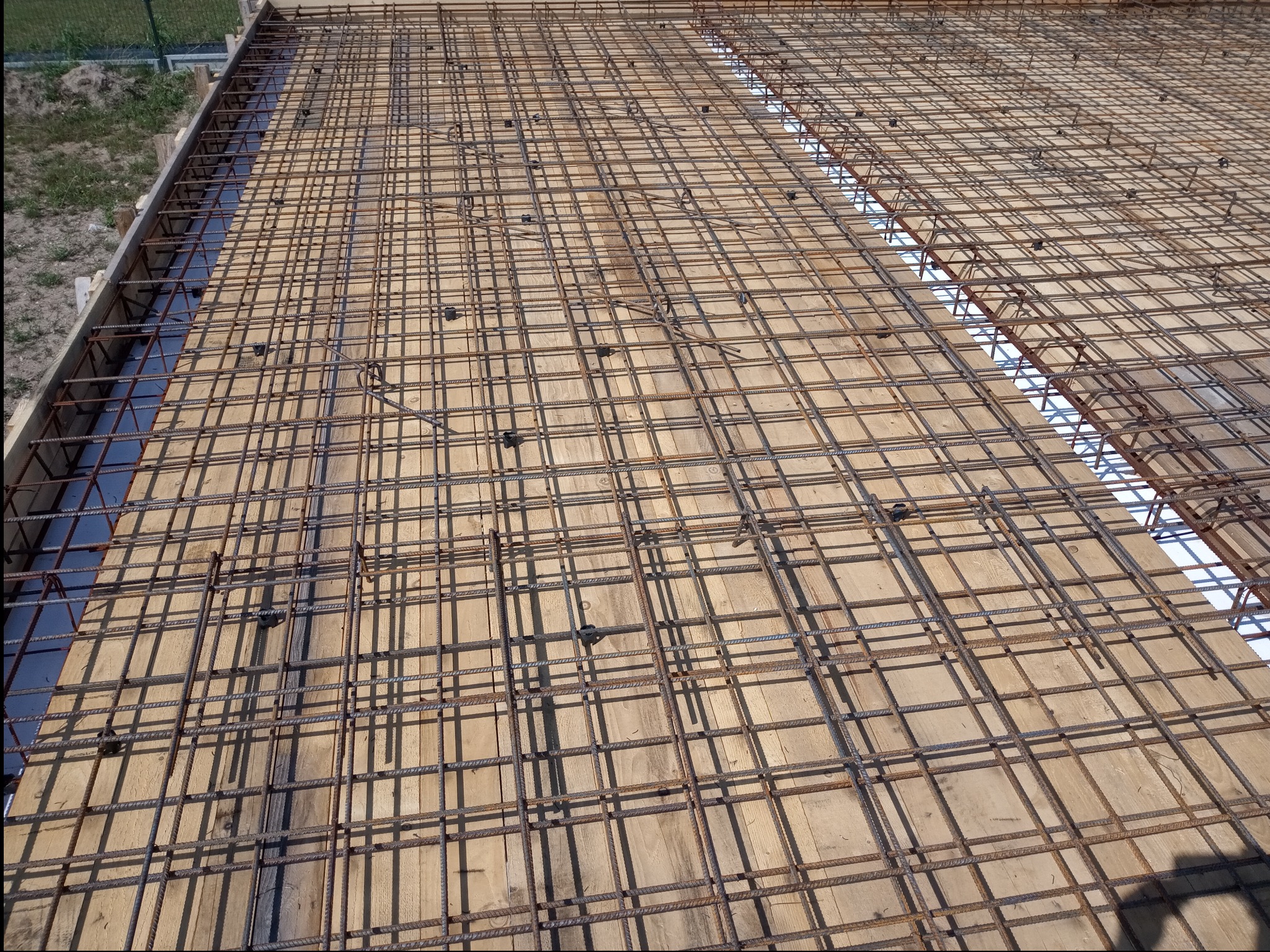 Zbrojenie ułożone na deskowaniu pod wylewkę betonową, widoczne dystanse z tworzywa sztucznego, przygotowane do zalania betonem.