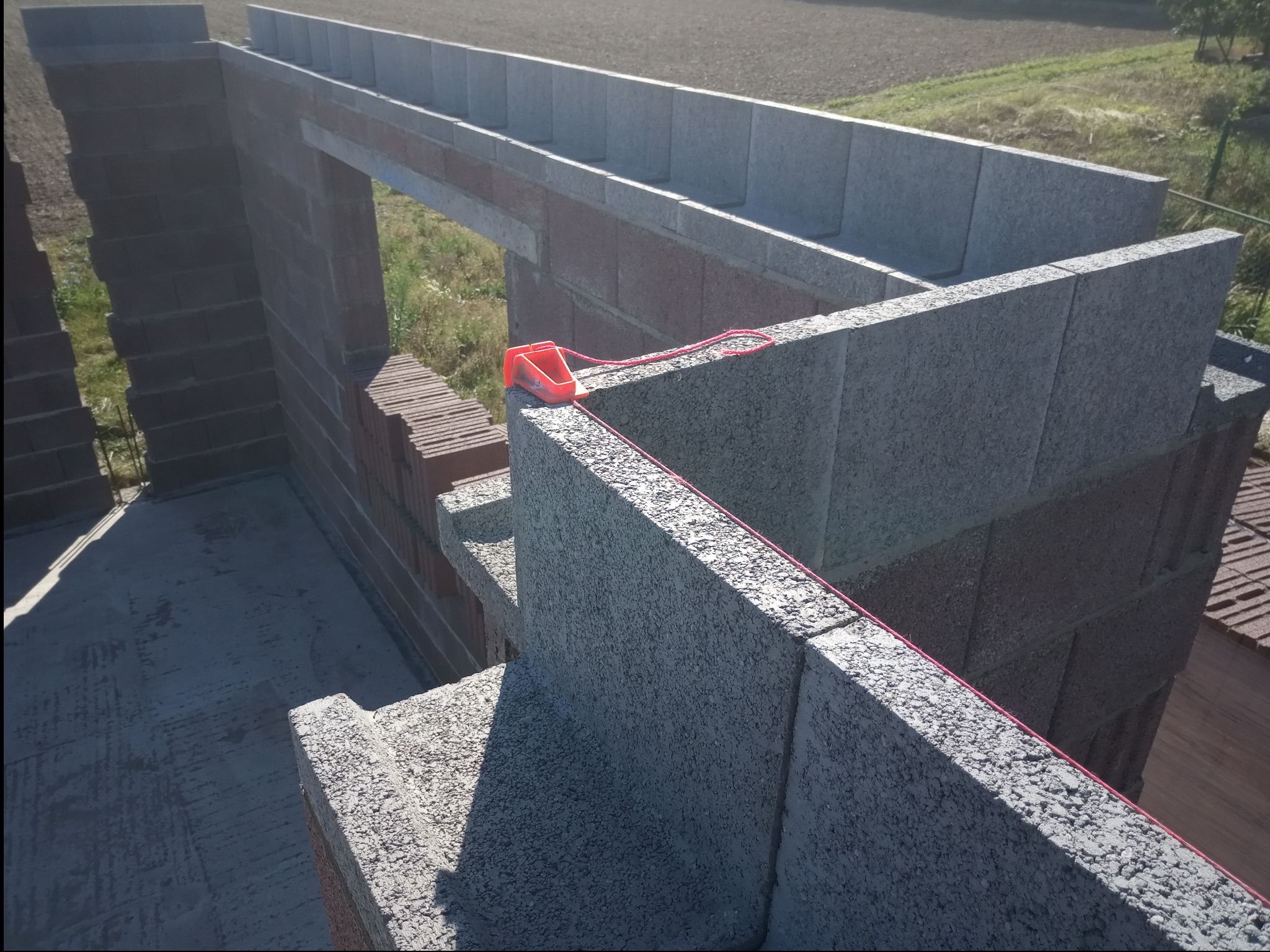 Wznoszenie ścian domu z bloczków betonowych i cegły ceramicznej, widoczne narzędzie murarskie - sznurek traserski z poziomnicą.