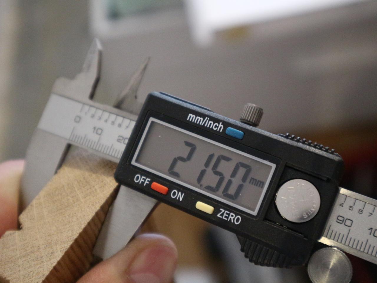 Pomiar grubości drewnianego elementu suwmiarką cyfrową, wskazanie 21.50 mm, widoczny przekrój drewna z usłojeniem.