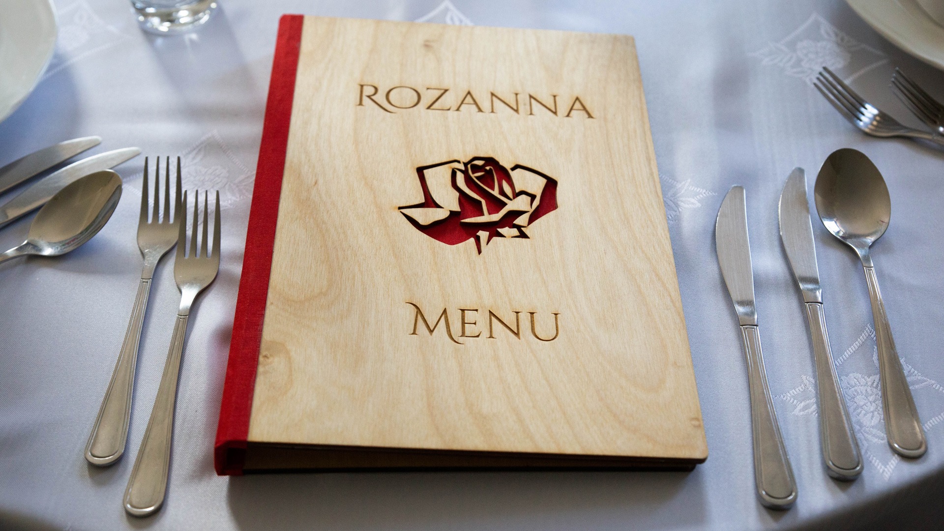 Drewniane menu restauracji 'Rozanna' z wygrawerowanym motywem róży na stole z nakryciem.
