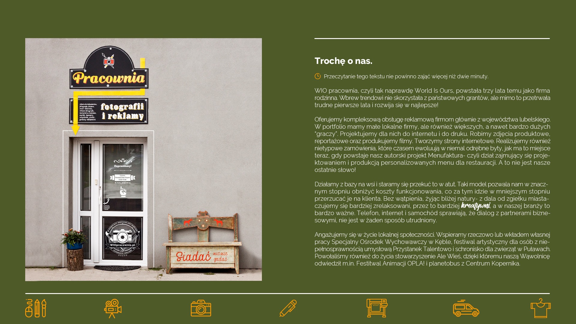 Fasada budynku z szyldem 'Pracownia fotografii i reklamy', drzwi wejściowe z naklejką informacyjną i logo firmy, obok drewniana ławeczka z napisem 'Siadać nie gadać', doniczka z kwiatami.