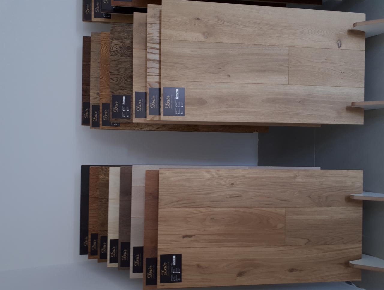 Ekspozycja próbek podłogowych paneli i parkietów w różnych odcieniach drewna, z etykietami producenta, umieszczonych na półkach w sklepie.