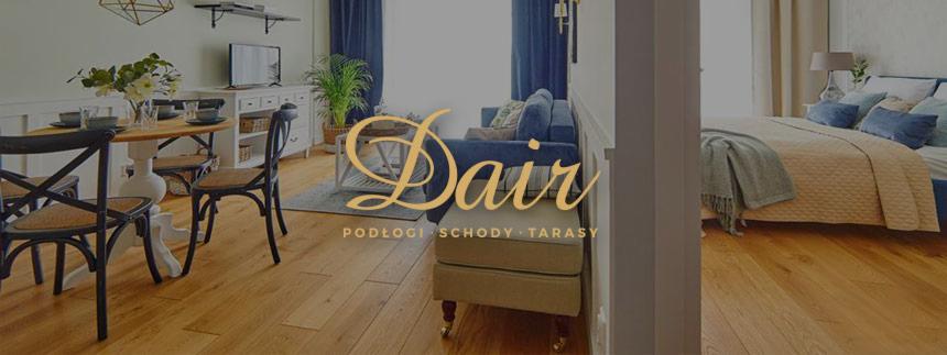 Jasna, drewniana podłoga w otwartym planie mieszkania z widokiem na salon z sofą i sypialnię z łóżkiem, widoczny stół z krzesłami i dekoracjami, nałożone logo firmy.