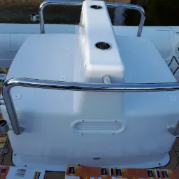 Biały kokpit łodzi motorowej z chromowanymi relingami i uchwytami na napoje; podłoga wyłożona panelami, na podłodze leżą kartony i arkusze z kolorami.