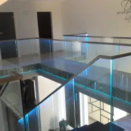 Nowoczesna szklana balustrada z podświetleniem LED na schodach wewnątrz domu, widok z góry, z napisem dekoracyjnym na ścianie w tle.