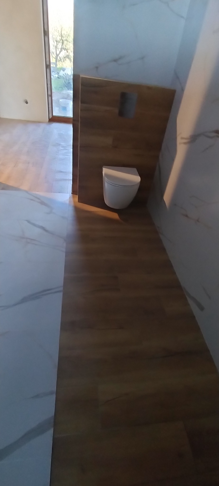 Nowoczesna łazienka z podwieszaną toaletą, drewnopodobnymi panelami ściennymi i marmurową podłogą, widok z góry, naturalne światło wpadające przez okno.