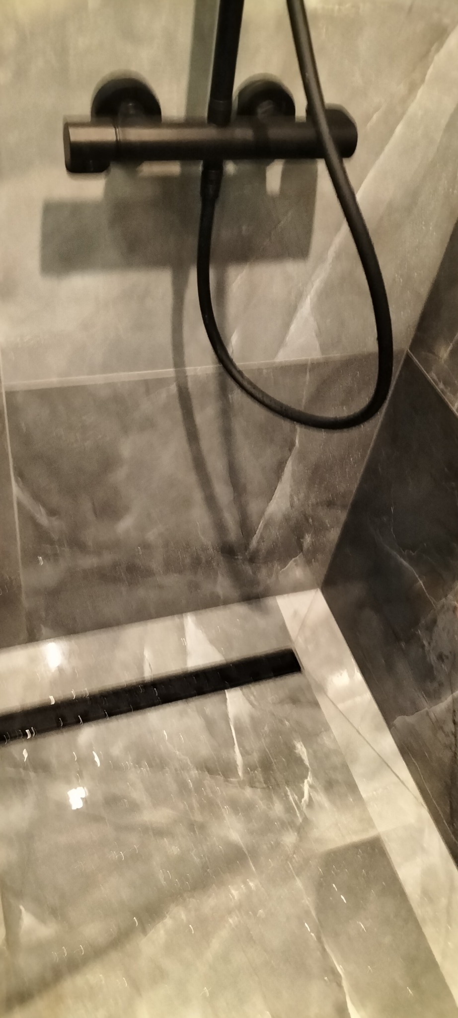 Czarny zestaw prysznicowy z deszczownicą i baterią termostatyczną na tle szarych płytek imitujących marmur w wykończonej łazience.