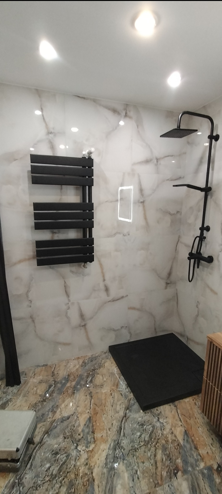 Wykończona łazienka z marmurowymi płytkami, czarną armaturą, grzejnikiem drabinkowym i brodzikiem typu slim.