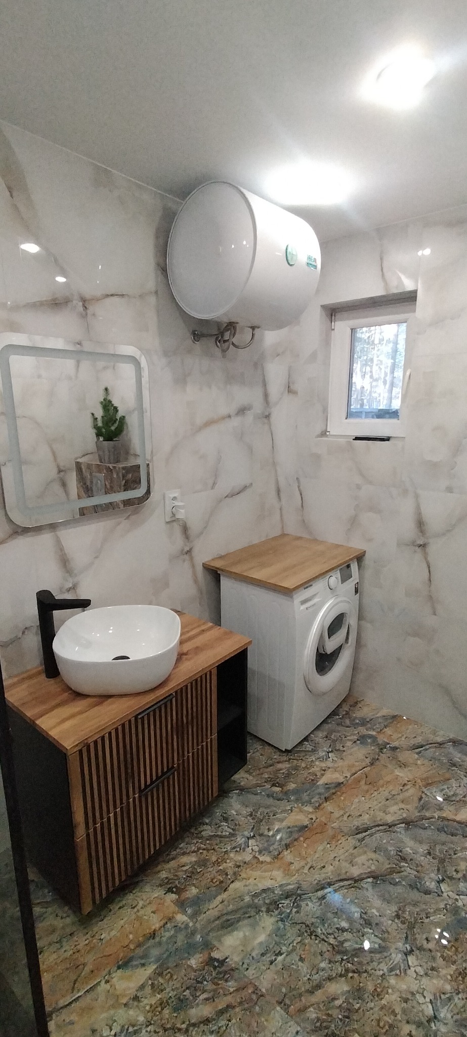 Nowoczesna łazienka z umywalką nablatową na szafce z lamelami, pralką z drewnianym blatem i marmurowymi płytkami na ścianach i podłodze.