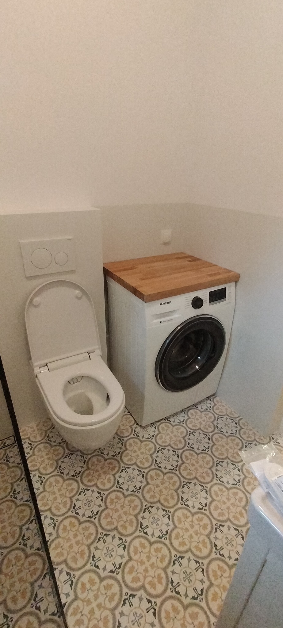 Toaleta z deską wolnoopadającą obok pralki Samsung z drewnianym blatem w łazience w Maciejowicach, z wzorzystą, beżowo-szarą podłogą.