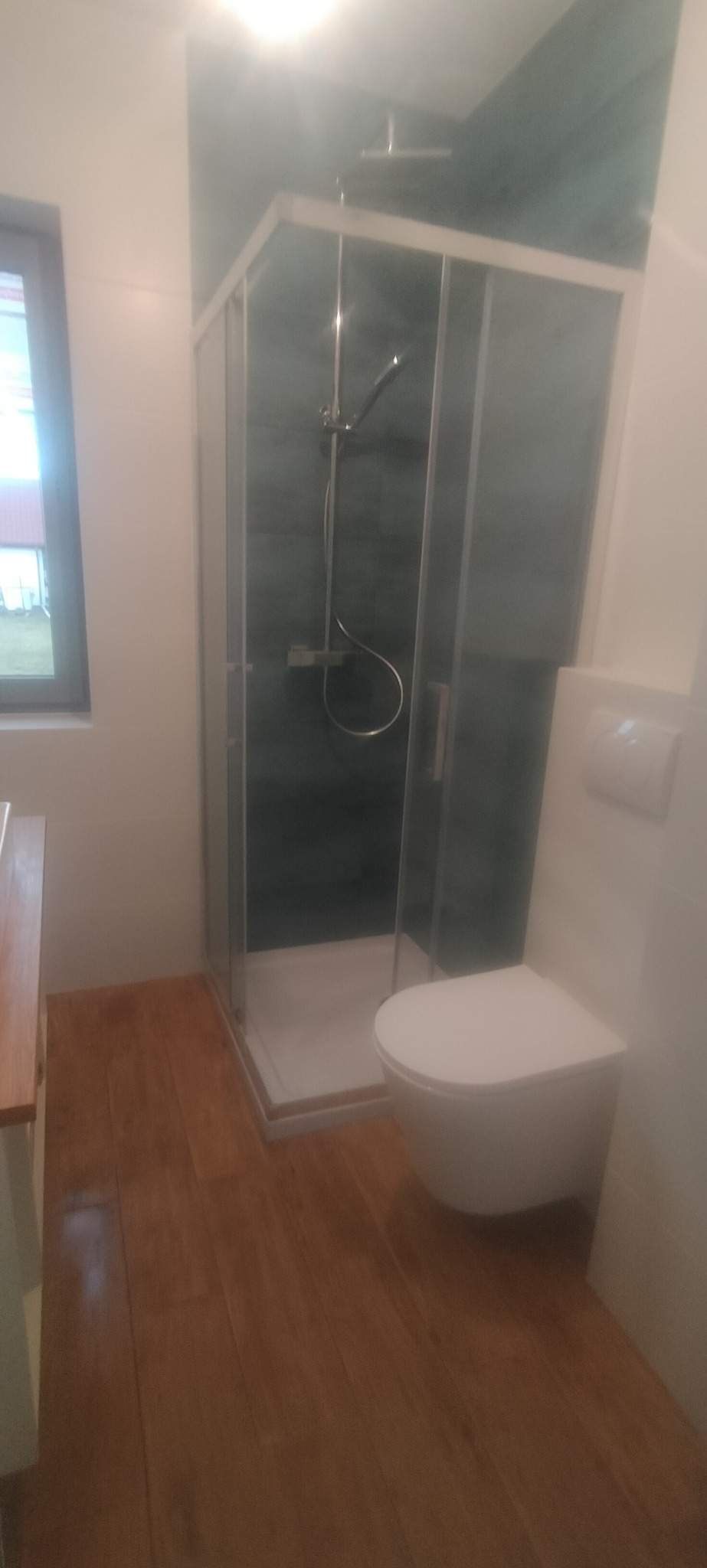 Nowoczesna łazienka z kabiną prysznicową, wiszącą toaletą i drewnopodobną podłogą, widok z perspektywy drzwi.