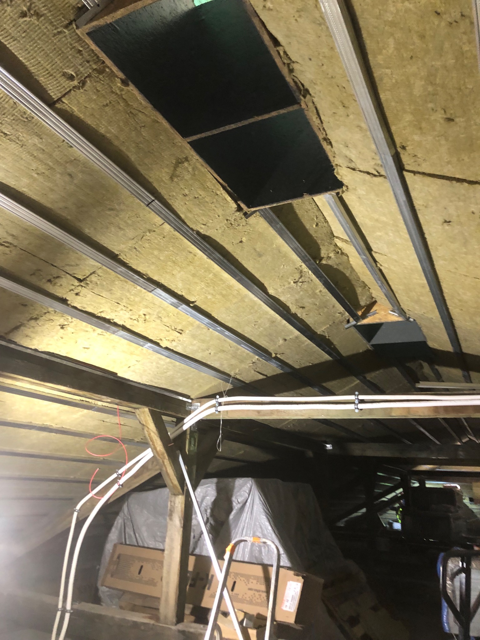 Montaż sufitu podwieszanego z wełną mineralną, widoczne profile metalowe, otwór wentylacyjny i częściowo widoczne instalacje elektryczne w poddaszu.