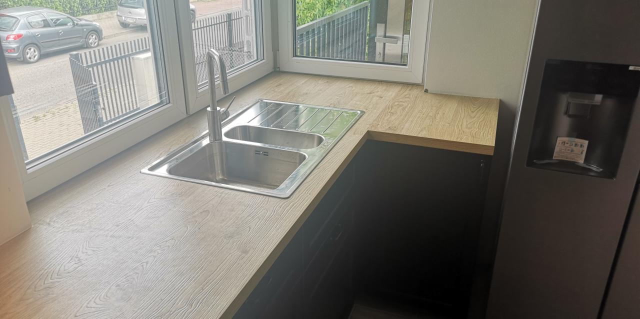 Kuchenny blat drewniany z dwukomorowym zlewem stalowym pod oknem, widok na ulicę z szarą zabudową i samochodem