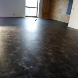 Ciemna podłoga z paneli w surowym wnętrzu z oknem i ścianą wyłożoną płytą OSB.