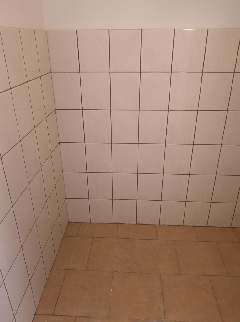 Wnętrze narożnika łazienki wyłożonego jasnymi, kwadratowymi płytkami ściennymi z ciemnymi fugami i brązowymi płytkami podłogowymi.