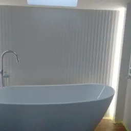 Nowoczesna, wolnostojąca wanna z chromowaną armaturą na tle ściany z pionowymi panelami dekoracyjnymi i oświetleniem LED.