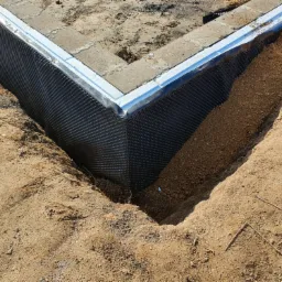 Fundament domu z izolacją przeciwwilgociową z folii kubełkowej i obłożony piaskiem, widoczne detale łączenia izolacji.