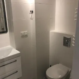 Nowoczesna, mała łazienka z białą armaturą, geometrycznymi płytkami podłogowymi i minimalistycznym oświetleniem punktowym.