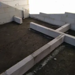 Wnętrze w trakcie budowy z widocznymi ścianami z betonu komórkowego i fundamentami, poziomowanie za pomocą sznurka.