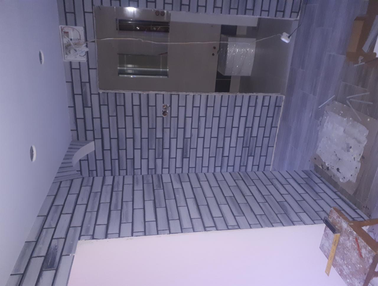 Świeżo ułożone szare cegiełki na ścianie w łazience, widoczne przygotowania do dalszych prac wykończeniowych, w tle lustro i elementy instalacji.