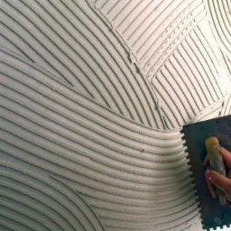 Nakładanie warstwy wyrównującej na ścianę w Strzelinie, widoczne ślady po pacy tworzące wzór fal i linii.