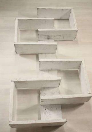 Białe, drewniane półki w kształcie schodów, przymocowane do ściany, z widocznymi śladami farby i naturalnego drewna, minimalistyczny design.