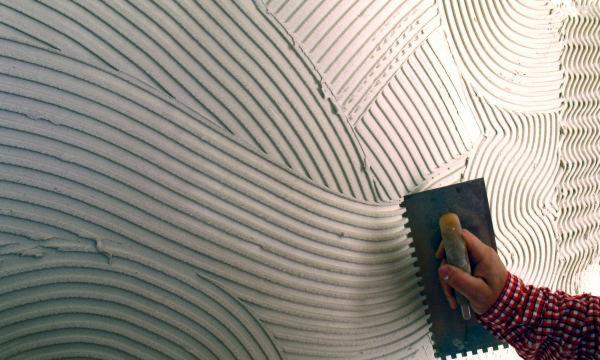 Nakładanie warstwy wyrównującej na ścianę w Strzelinie, widoczne ślady po pacy tworzące wzór fal i linii.