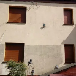 Fragment elewacji budynku z widocznym efektem częściowego czyszczenia, gdzie dolna część ściany jest jaśniejsza od górnej, z wysuniętą lancą do czyszczenia elewacji po lewej stronie.