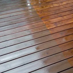 Częściowo wyczyszczony drewniany taras, ukazujący różnicę w wyglądzie przed i po zabiegu, z widocznymi kroplami wody.