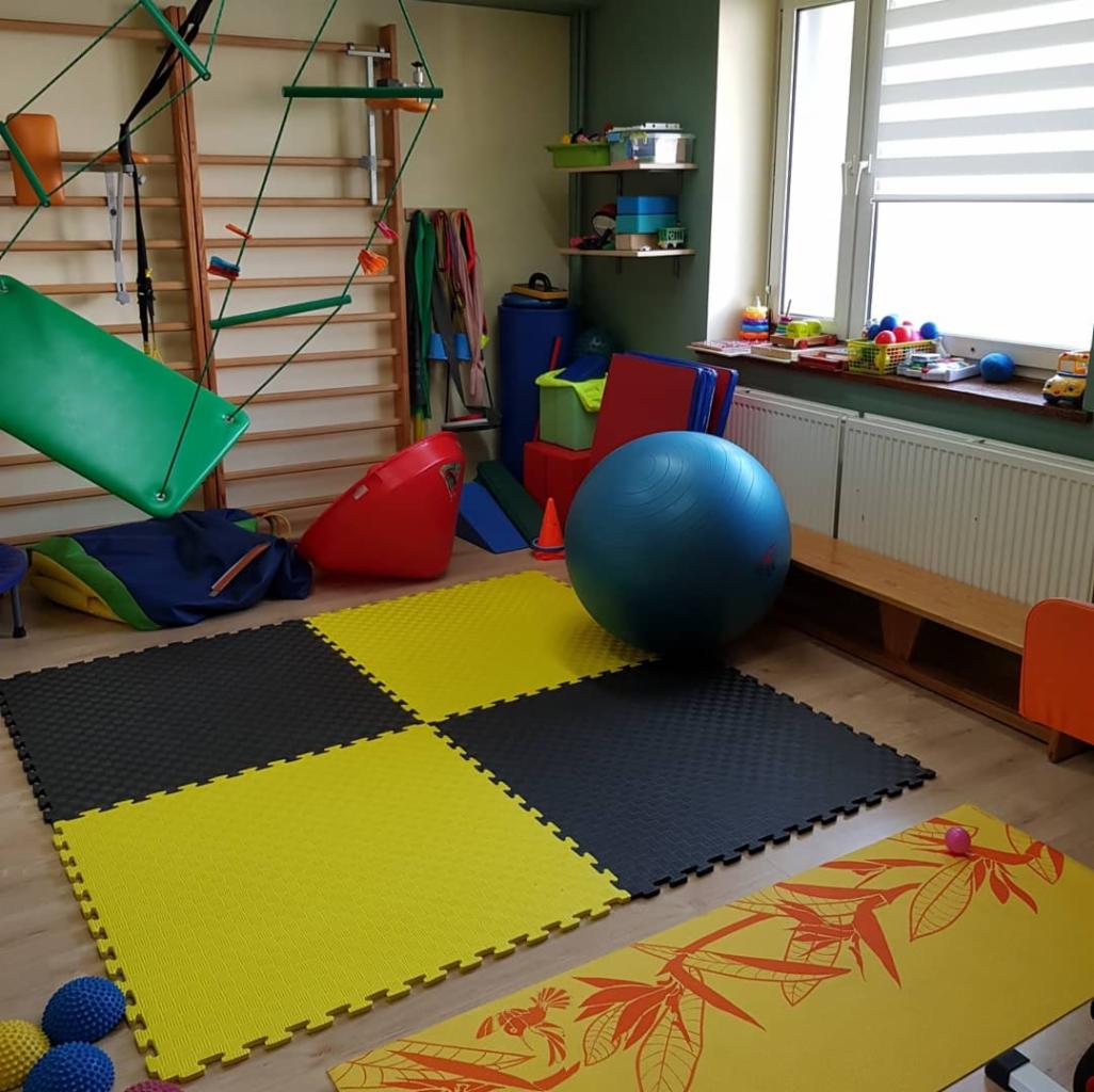 Sala do ćwiczeń z drabinką gimnastyczną, huśtawką, piłką rehabilitacyjną, matami podłogowymi w szachownicę i innymi przyborami.