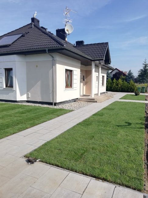 Nowo założony trawnik z rolki przy domu jednorodzinnym w Zielątkowie, z widocznymi szarymi płytami chodnikowymi i starannie ułożonym obrzeżem trawnika.