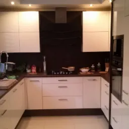 Nowoczesna kuchnia w kształcie litery U z białymi, lakierowanymi frontami szafek i ciemnobrązowym blatem, wyposażona w płytę grzewczą, piekarnik i okap, z widocznymi akcesoriami kuchennymi.