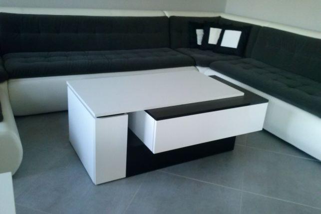 Nowoczesny stolik kawowy w kolorach bieli i czerni z wysuwaną szufladą, dopasowany do narożnej sofy z ciemną tapicerką.