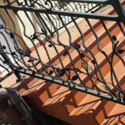 Kute, czarne balustrady z motywem roślinnym na tle schodów z terakoty, widoczne elementy orynnowania.