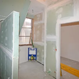 Łazienka w trakcie remontu: widoczne płyty gipsowo-kartonowe na ścianach, częściowo wyszpachlowane, z widocznymi instalacjami wodno-kanalizacyjnymi i stelażem podtynkowym WC.