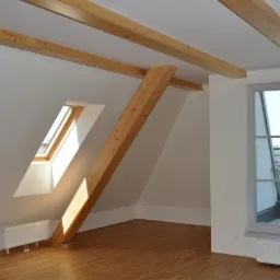 Jasne poddasze w Czarnkowie z drewnianymi belkami stropowymi, oknem dachowym i dużym oknem balkonowym, świeżo pomalowane na biało, z drewnianą podłogą.