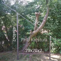 Spawana konstrukcja metalowa, rury o przekroju kwadratowym, wkomponowana w naturalne otoczenie drzew i zieleni, z widocznymi wymiarami rur naniesionymi na zdjęcie.