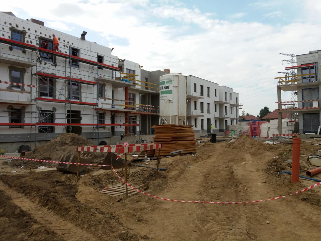 Budowa wielorodzinnego budynku mieszkalnego w trakcie ocieplania, widoczne rusztowania, styropian, materiały budowlane i teren budowy.