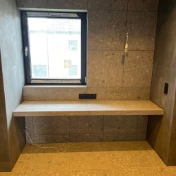 BARTOSZ SOPEL - Wykończona wnęka okienna z blatem i płytkami w odcieniach szarości i beżu. Widoczne gniazdka elektryczne i fragment instalacji oświetleniowej.