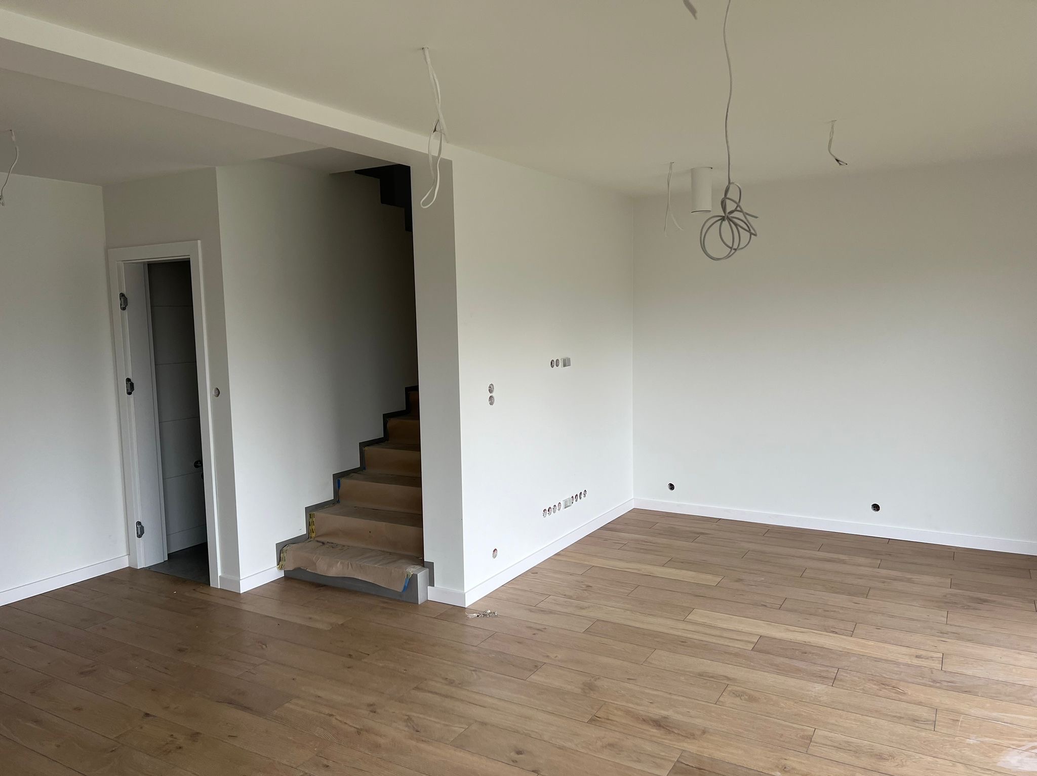 Jasne wnętrze po remoncie: świeżo pomalowane ściany, ułożone panele podłogowe, schody zabezpieczone folią, wystające kable elektryczne.