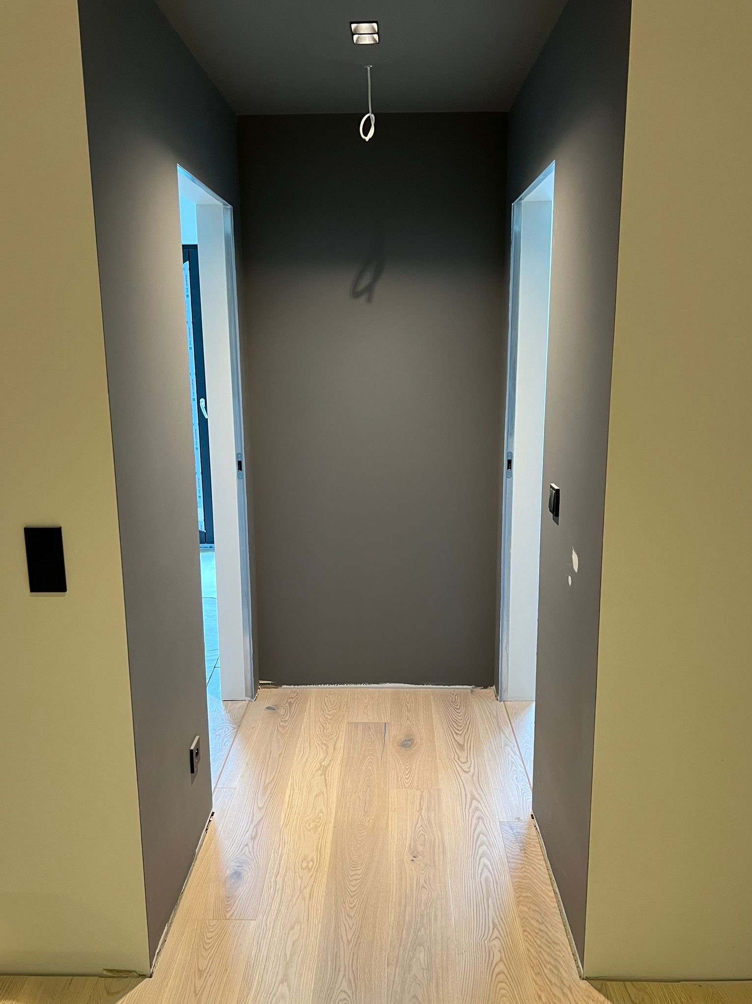 Korytarz po remoncie: świeżo pomalowane ściany w odcieniach szarości i beżu, jasna drewniana podłoga, widoczne dwa wejścia do pomieszczeń. Minimalistyczny design.