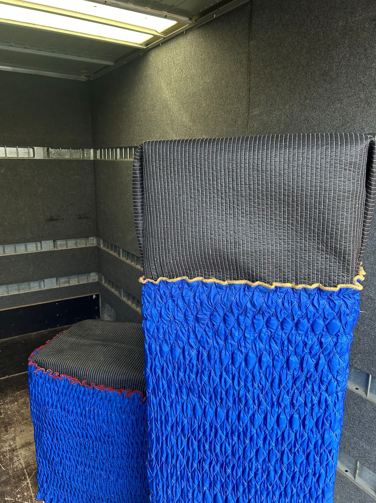 Zabezpieczone meble wewnątrz pojazdu transportowego. Krzesło i fotel owinięte w niebieską, pikowaną folię i szarą tkaninę w paski, gotowe do przeprowadzki.