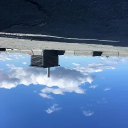 Metalowa konstrukcja wentylacyjna na dachu, widok z dołu na błękitne niebo z chmurami.