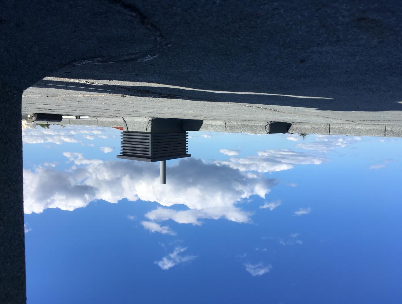 Metalowa konstrukcja wentylacyjna na dachu, widok z dołu na błękitne niebo z chmurami.